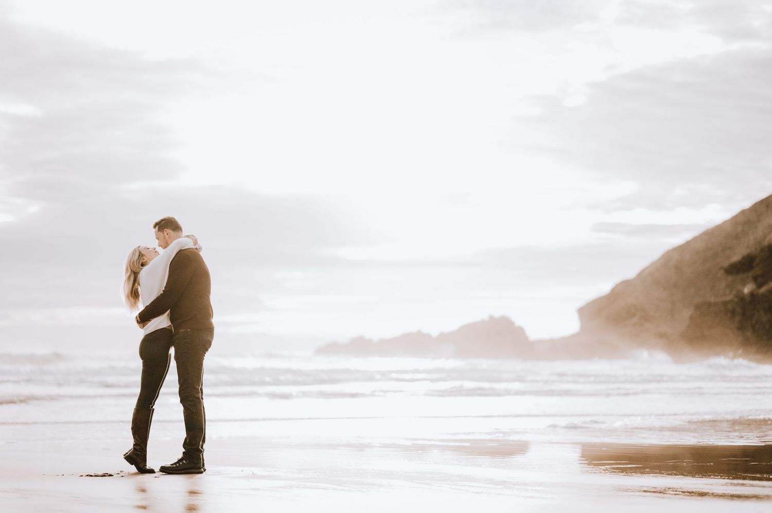 Silhouetted couple sharing an intimate moment on misty beach at sunset.