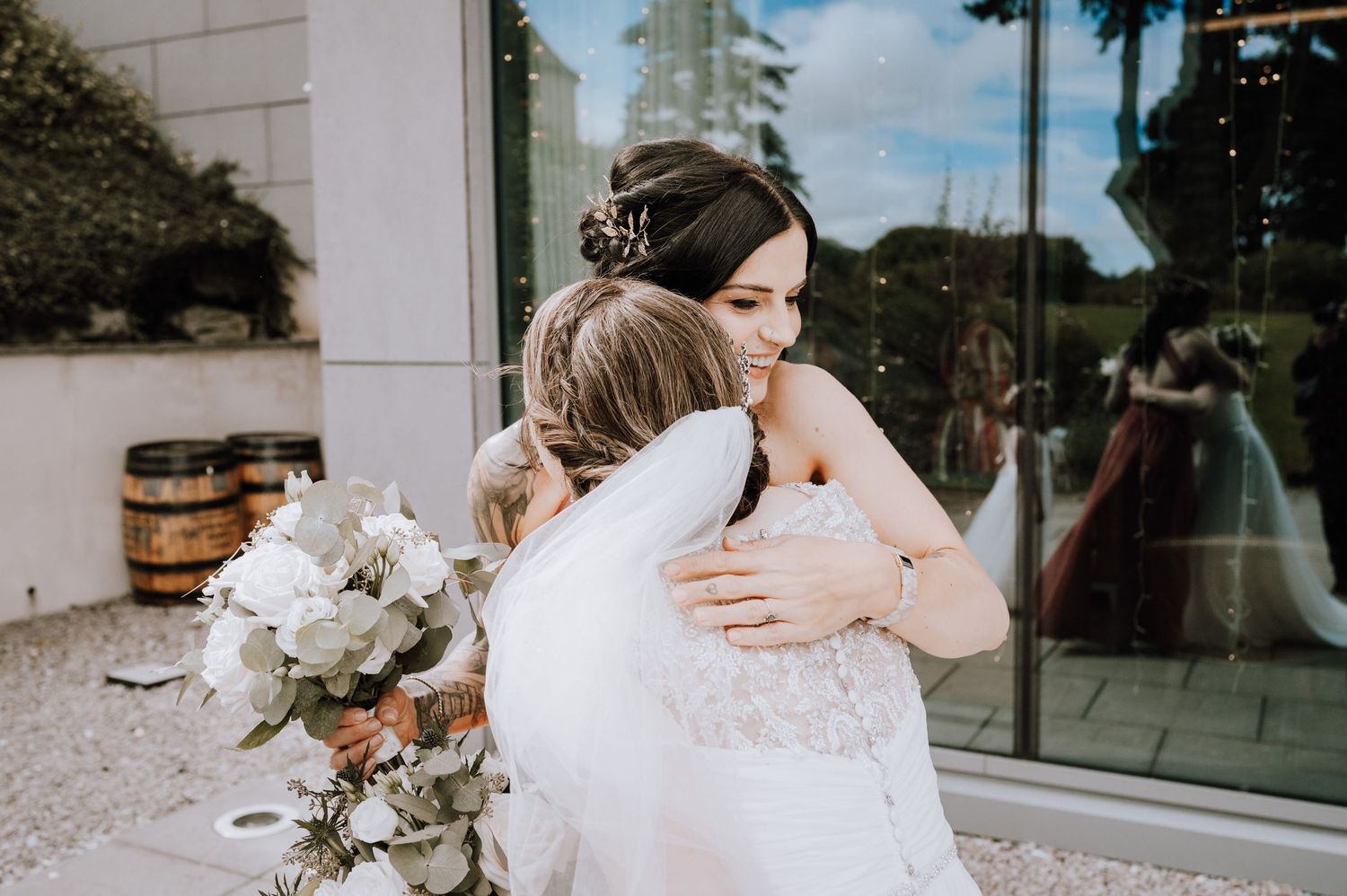 Emotional embrace between two people in white dresses with bouquet on ground.