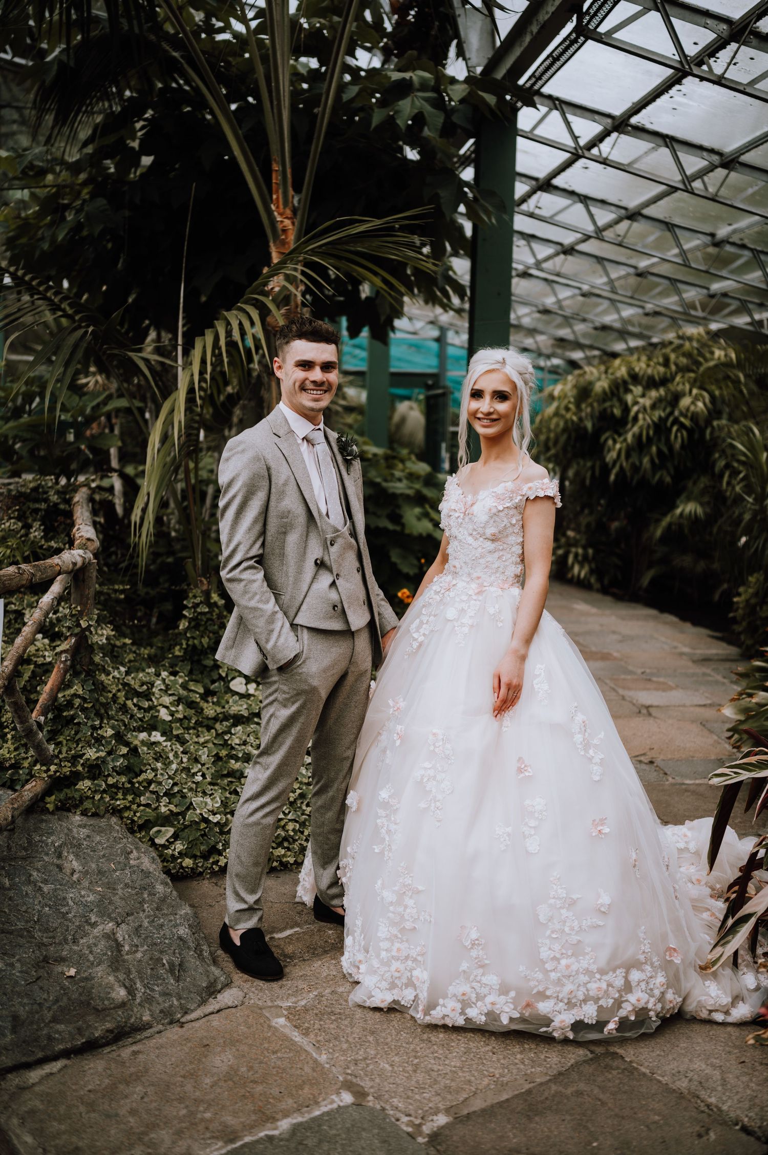 Wedding portrait in a greenhouse conservatory with tropical palm trees and stone pathway.