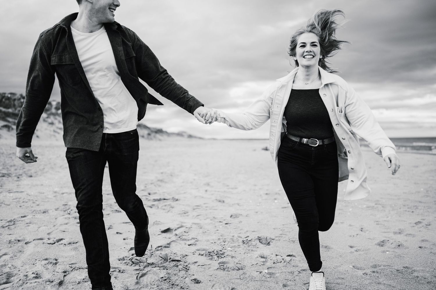 People walking and dancing together on a beach in black and white, creating a playful silhouette effect.