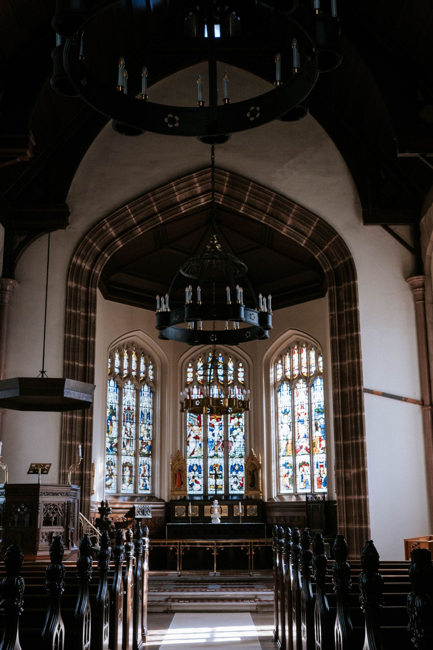 Interior view of a historic church with gothic stained glass windows and dark wooden beams.