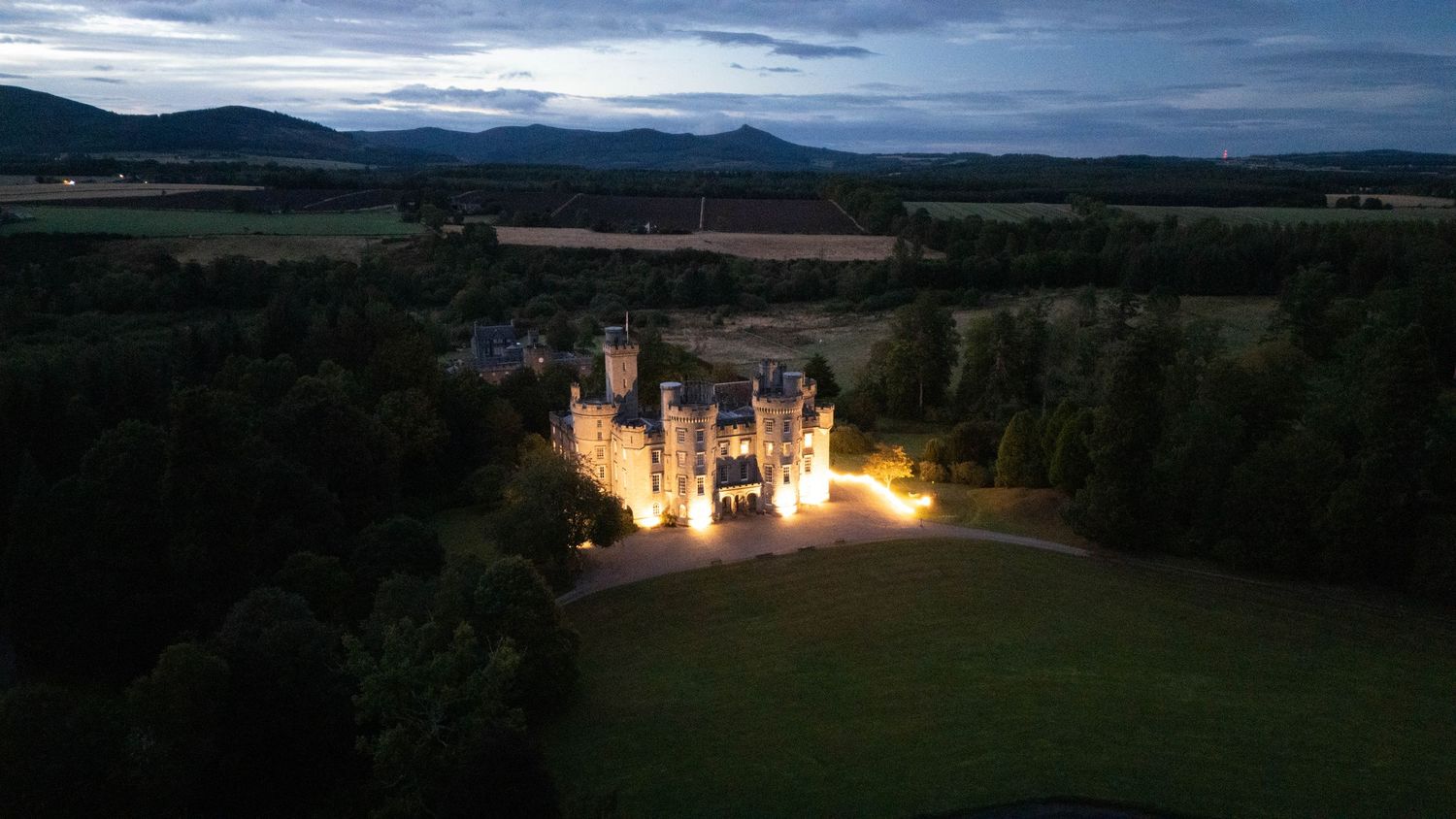 Panoramic view of a grand estate nestled in rolling countryside hills at dusk.