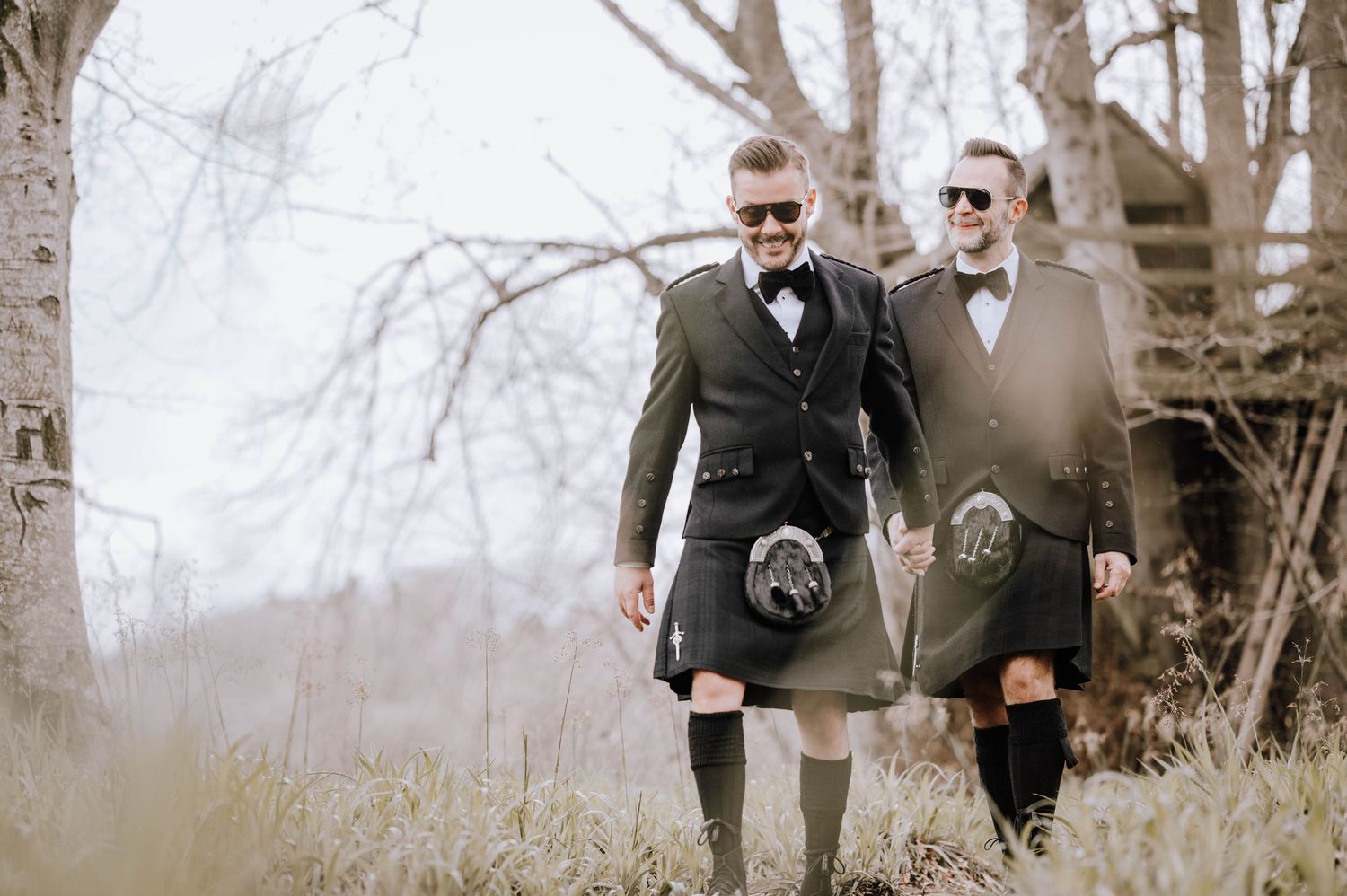 Logie House Wedding Photography. Two people in black tuxedos share a tender moment outdoors in nature.