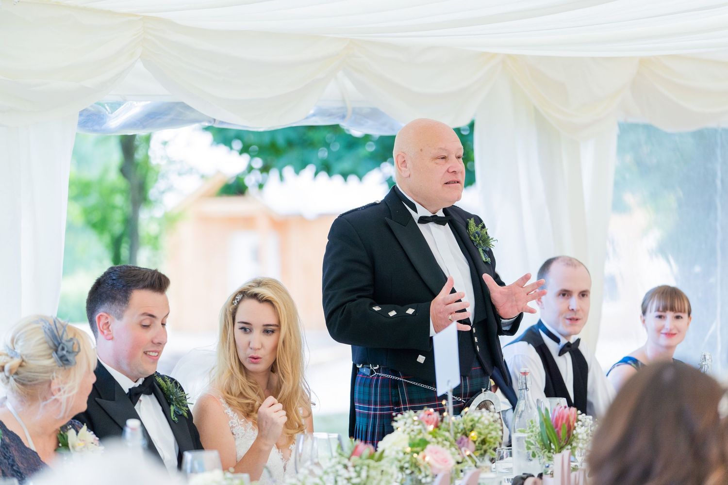 Wedding guests gathered at a formal reception with floral centerpieces and elegant table settings.
