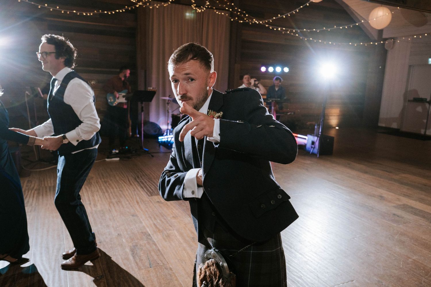 Wedding guests dancing and celebrating on wooden dance floor under fairy lights.