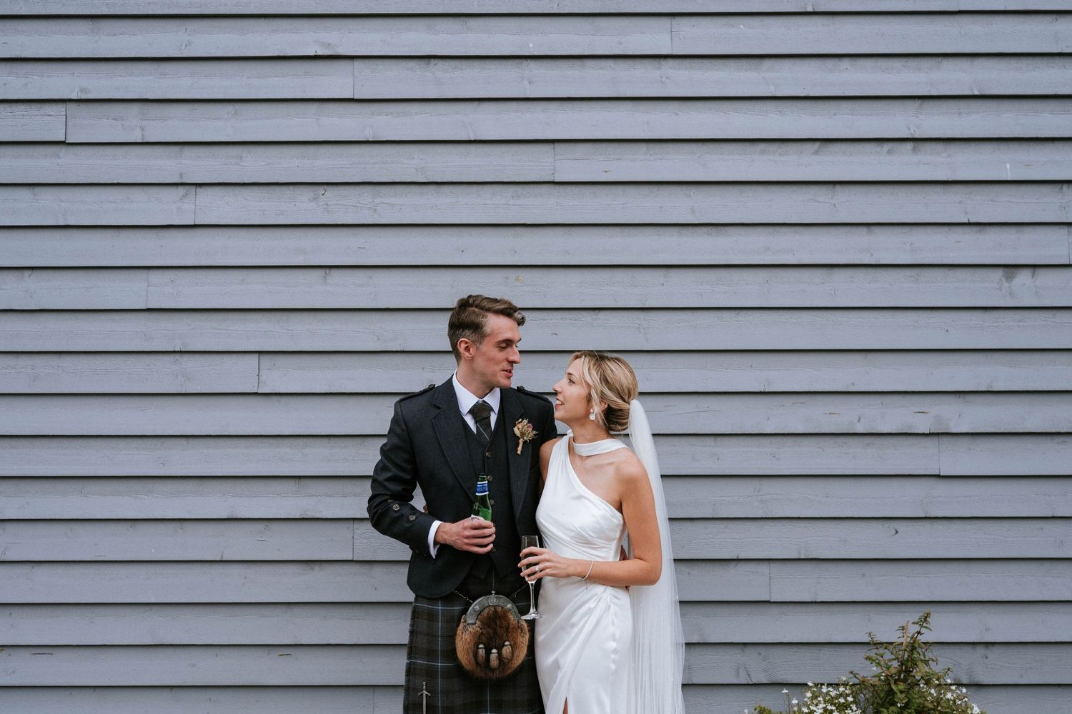 Wedding couple poses against grey wooden wall backdrop.