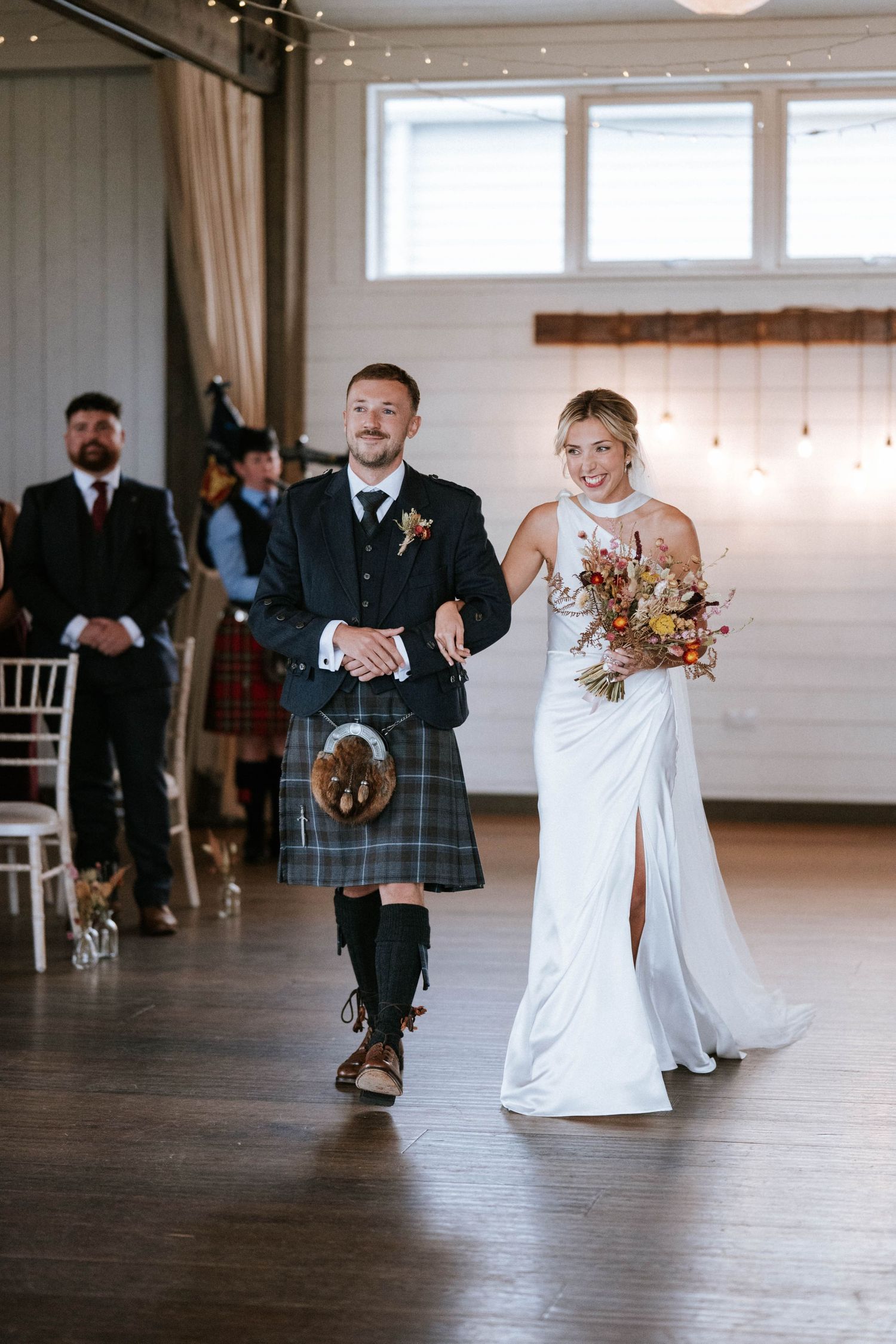 Couple shares first dance in bright rustic venue with string lights overhead.