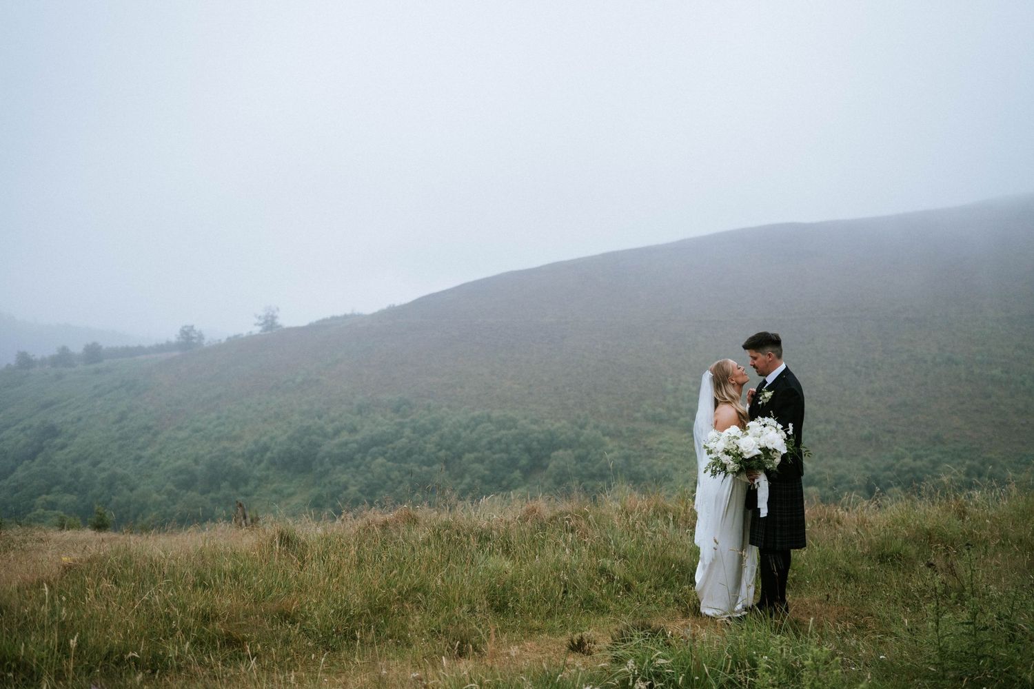 Ethereal wedding photos captured on a foggy mountainside with rolling hills in the background.