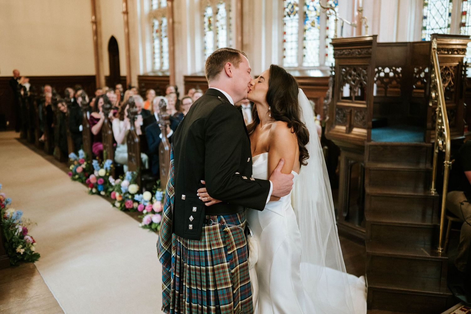 Romantic kiss during Scottish wedding ceremony with traditional kilt and white bridal gown.