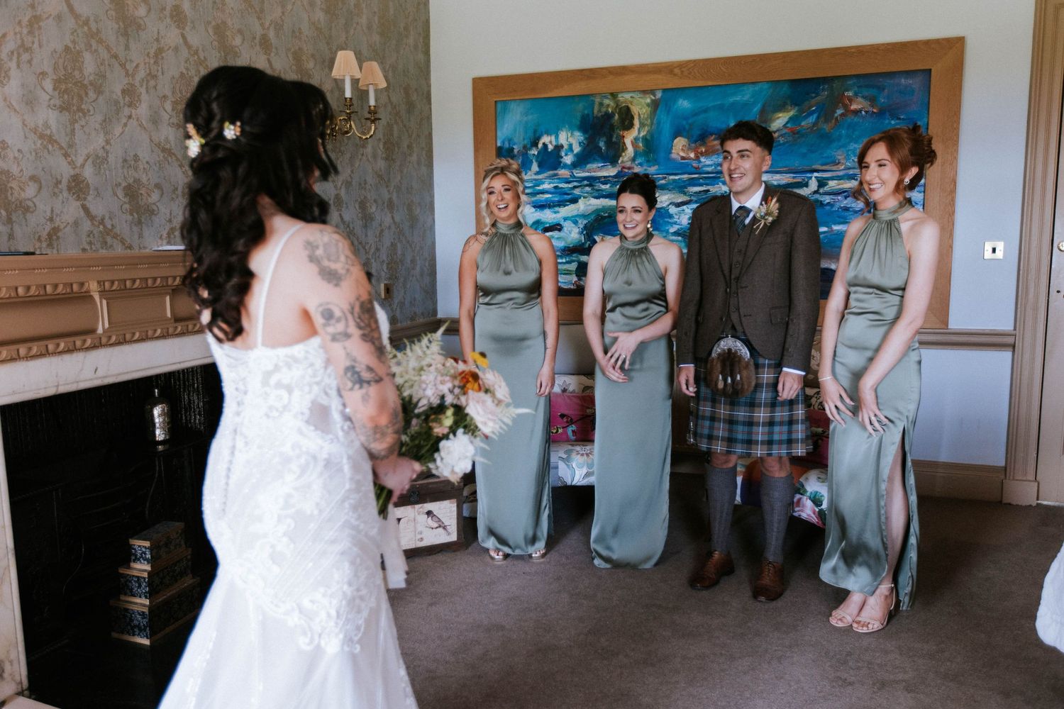 Wedding party in sage green dresses and Scottish formal wear poses for a group photo.