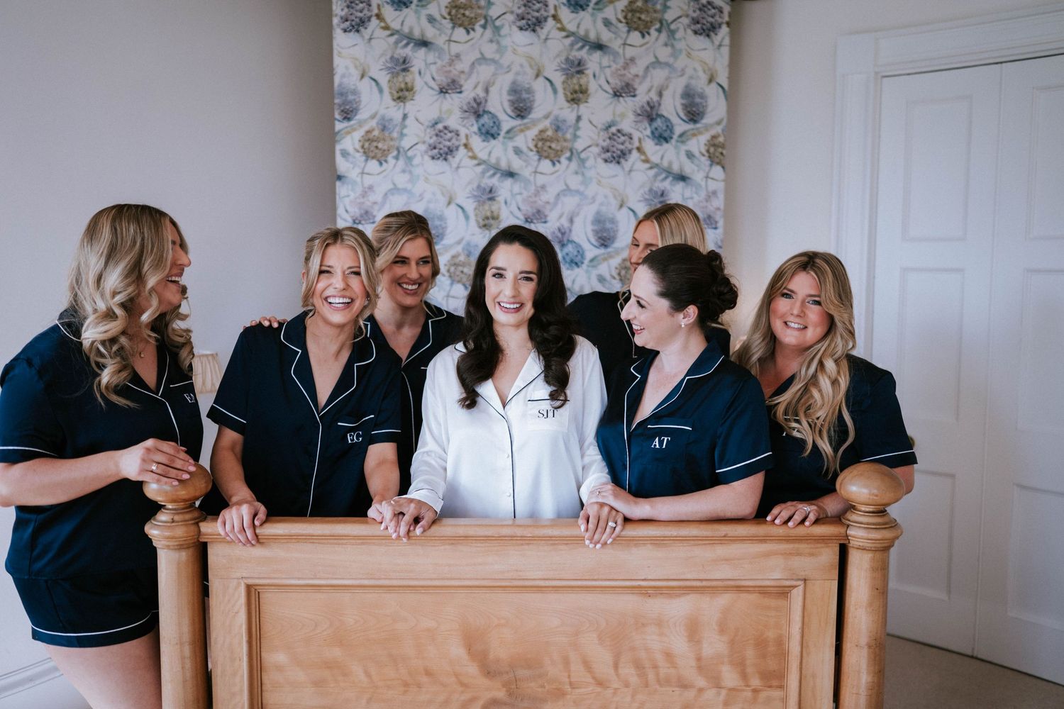 A group wearing matching navy sleepwear gather around a wooden bannister during pre-wedding preparations.