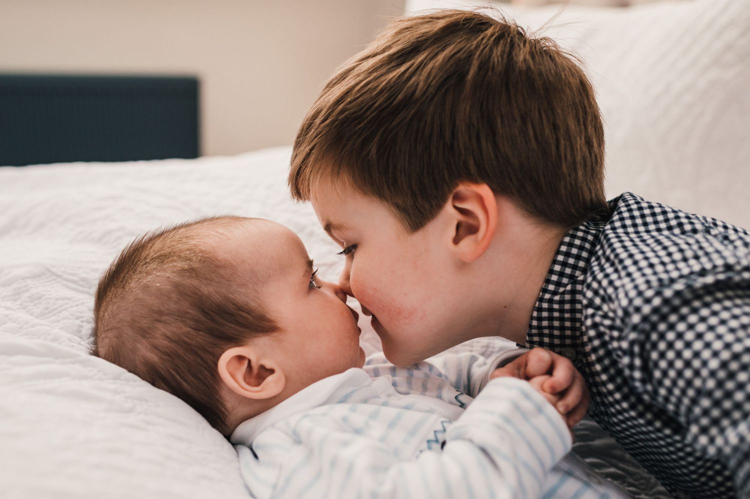 Siblings share a sweet moment together while lying down on a white bed.