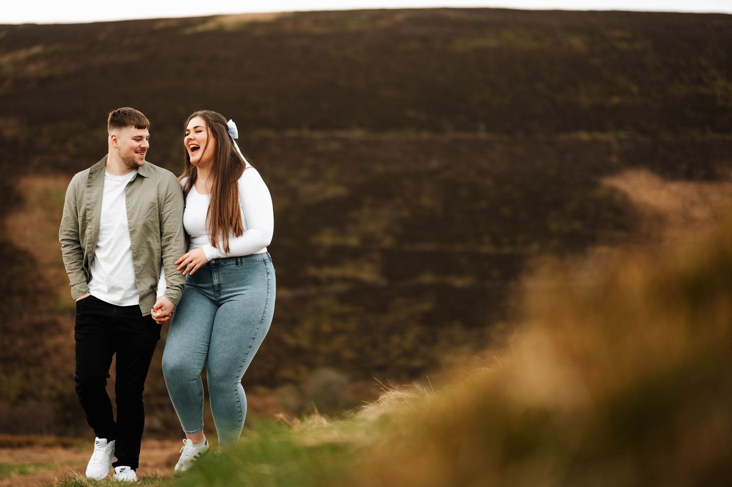 Couple walking together through golden grass field during sunset in romantic outdoor photoshoot.