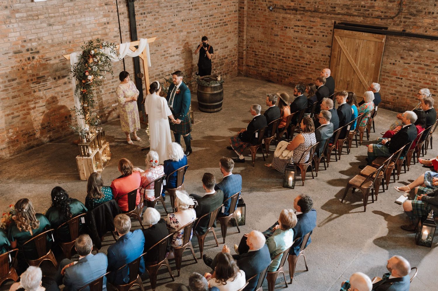 Aerial view of wedding ceremony in rustic brick venue with guests seated in angled rows.