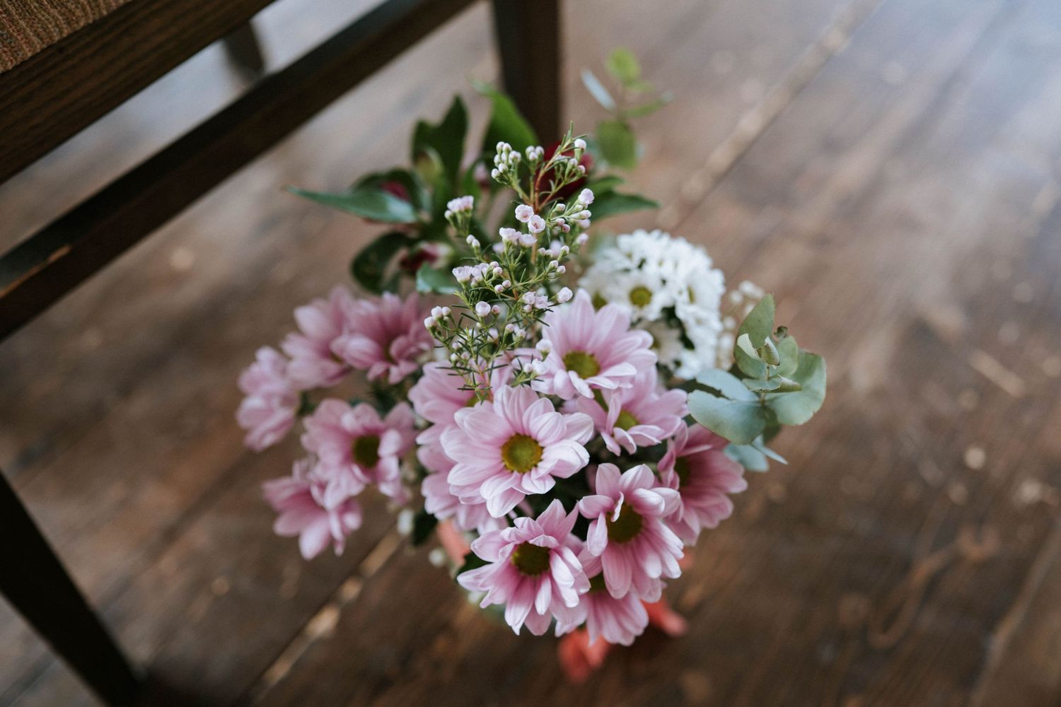 Pink chrysanthemum flowers with baby's breath arranged in rustic wooden setting.