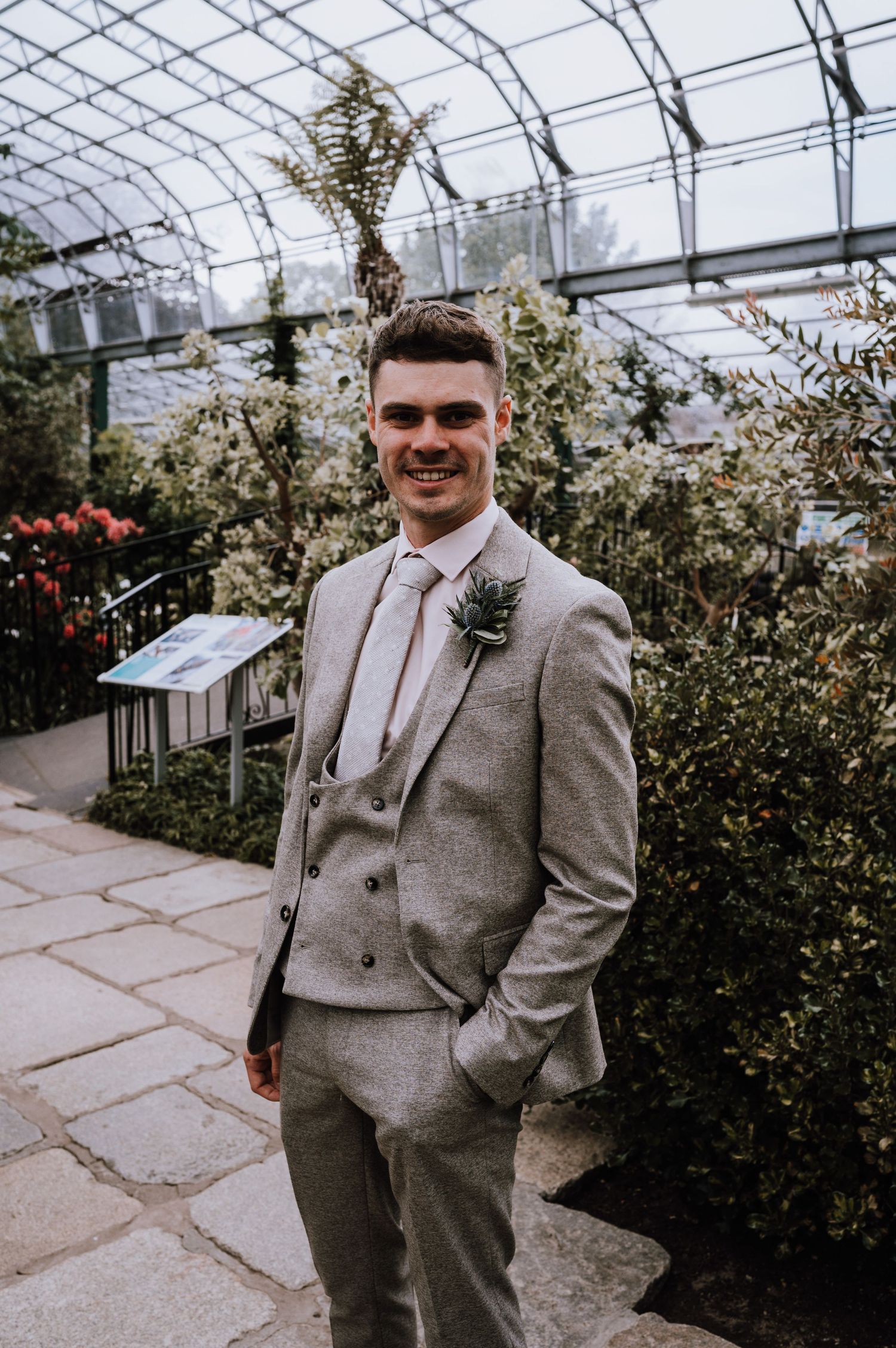 Wedding day portrait in a greenhouse setting with glass ceiling and surrounding plants.