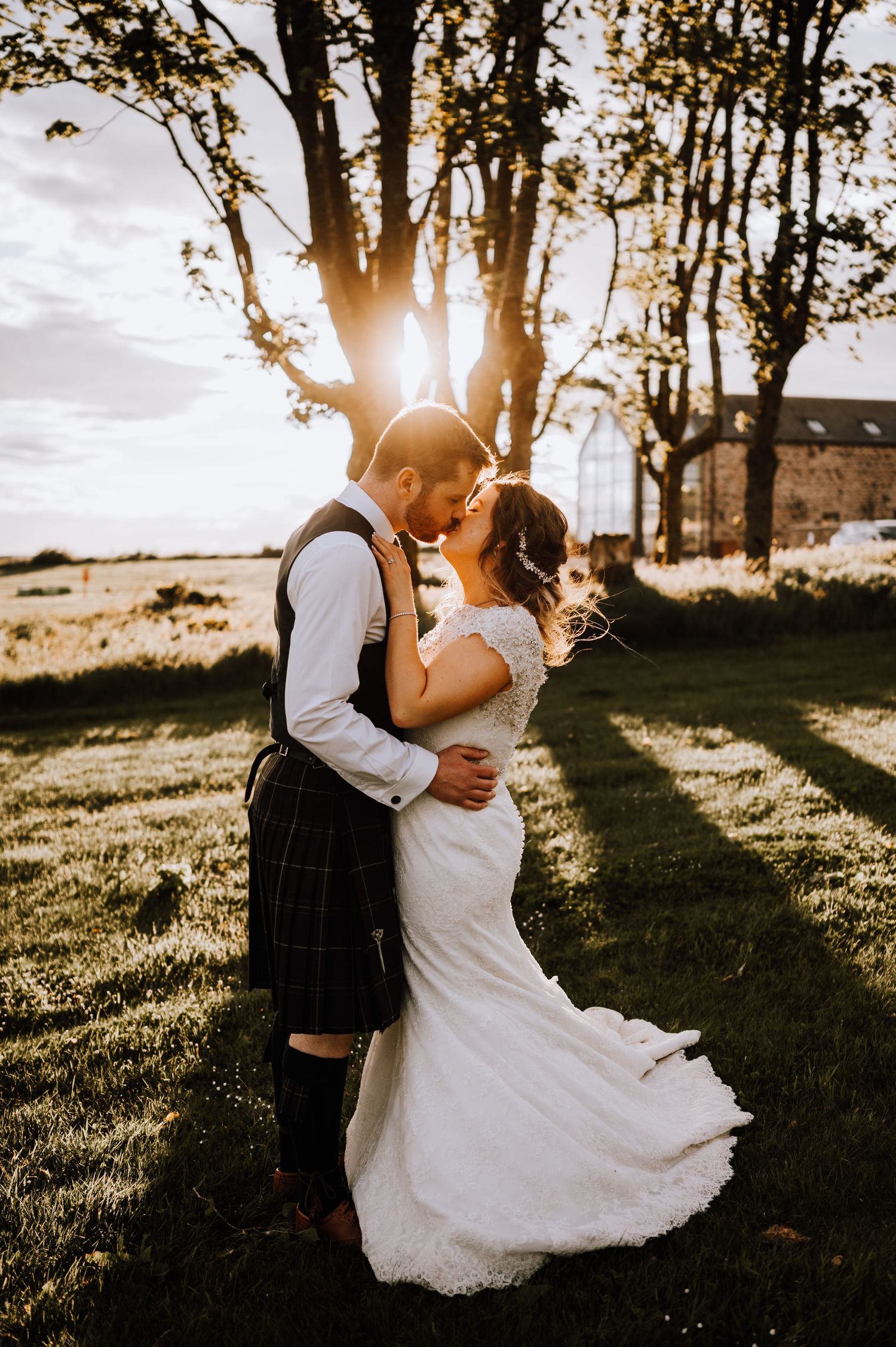 A romantic wedding couple embracing in golden sunset light with trees and greenery in the background.