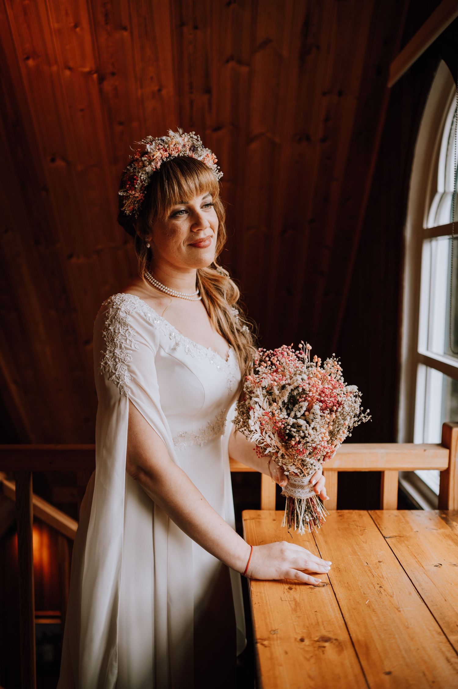 A wedding ceremony in a rustic wooden chapel with a person in a white dress and floral crown holding a pink bouquet.