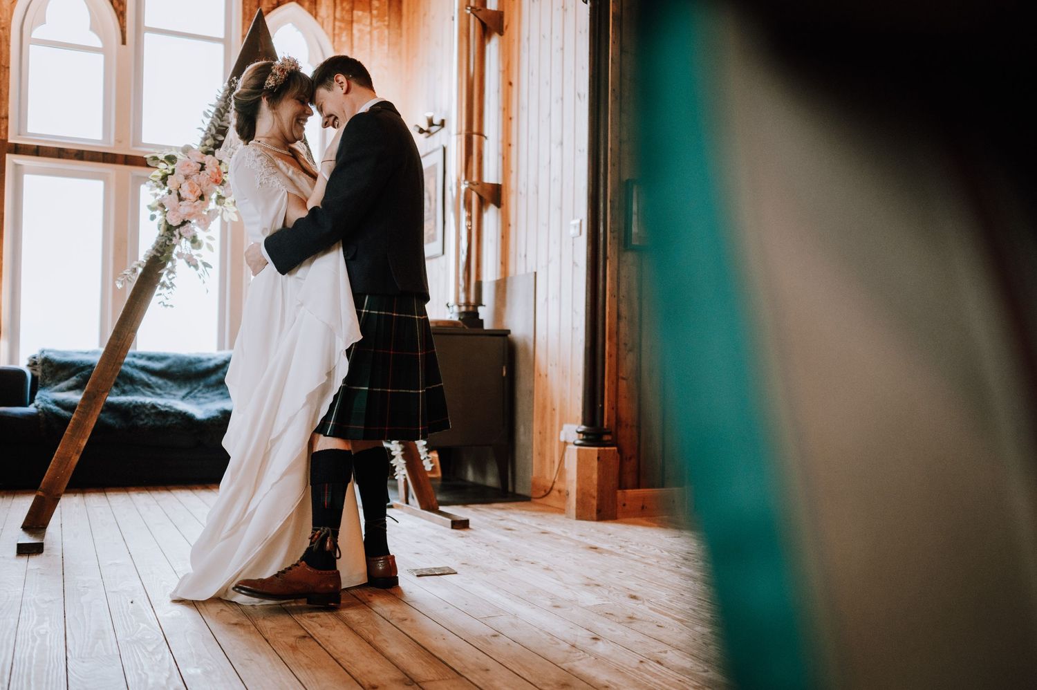 Intimate wedding dance moment captured in rustic venue with wooden floors and arched windows.