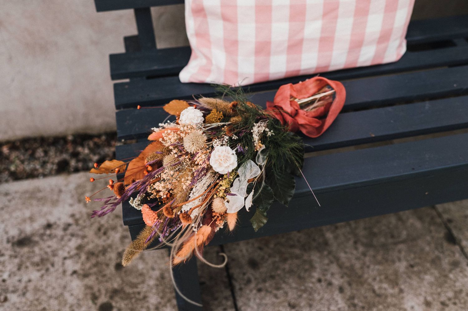 Rustic floral arrangement on a black bench with a gingham pillow.