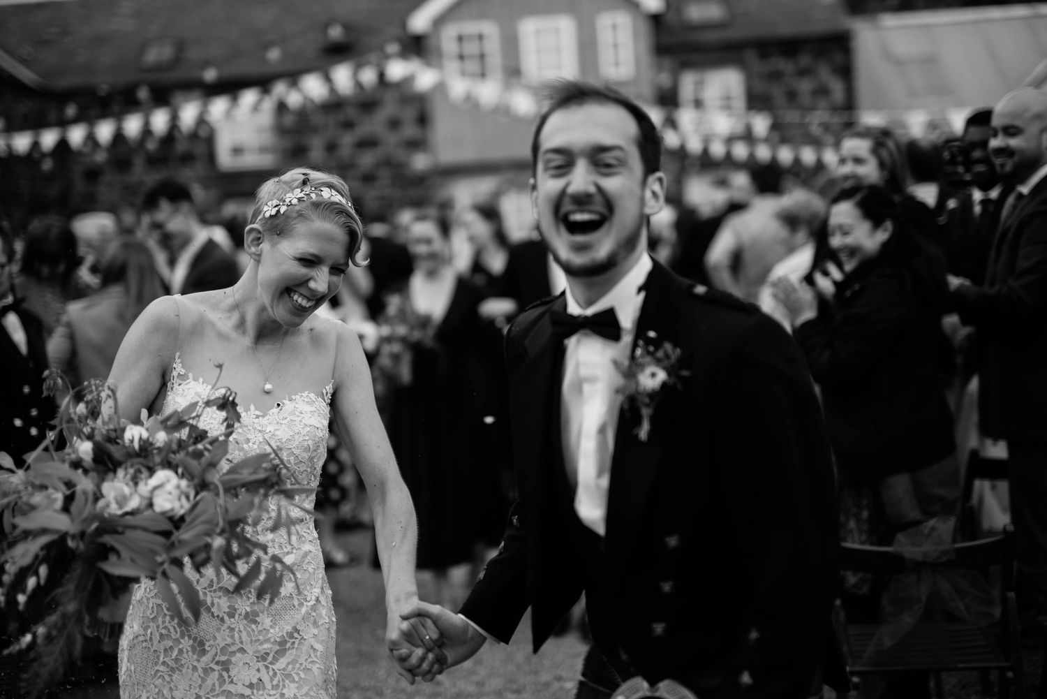 Black and white photo of newlyweds laughing during outdoor Scottish wedding celebration.