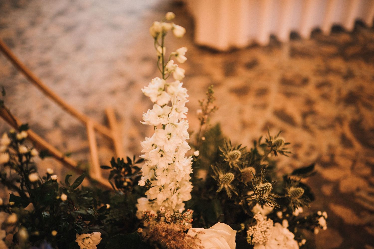 Delicate white floral stems and greenery arrangement illuminated by warm ambient lighting.