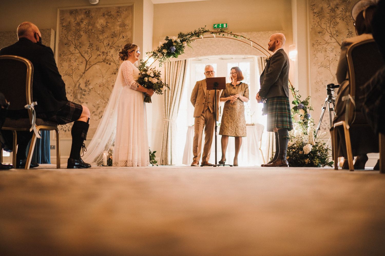 Wedding ceremony silhouette under an arch in an elegantly decorated room with floral wallpaper.