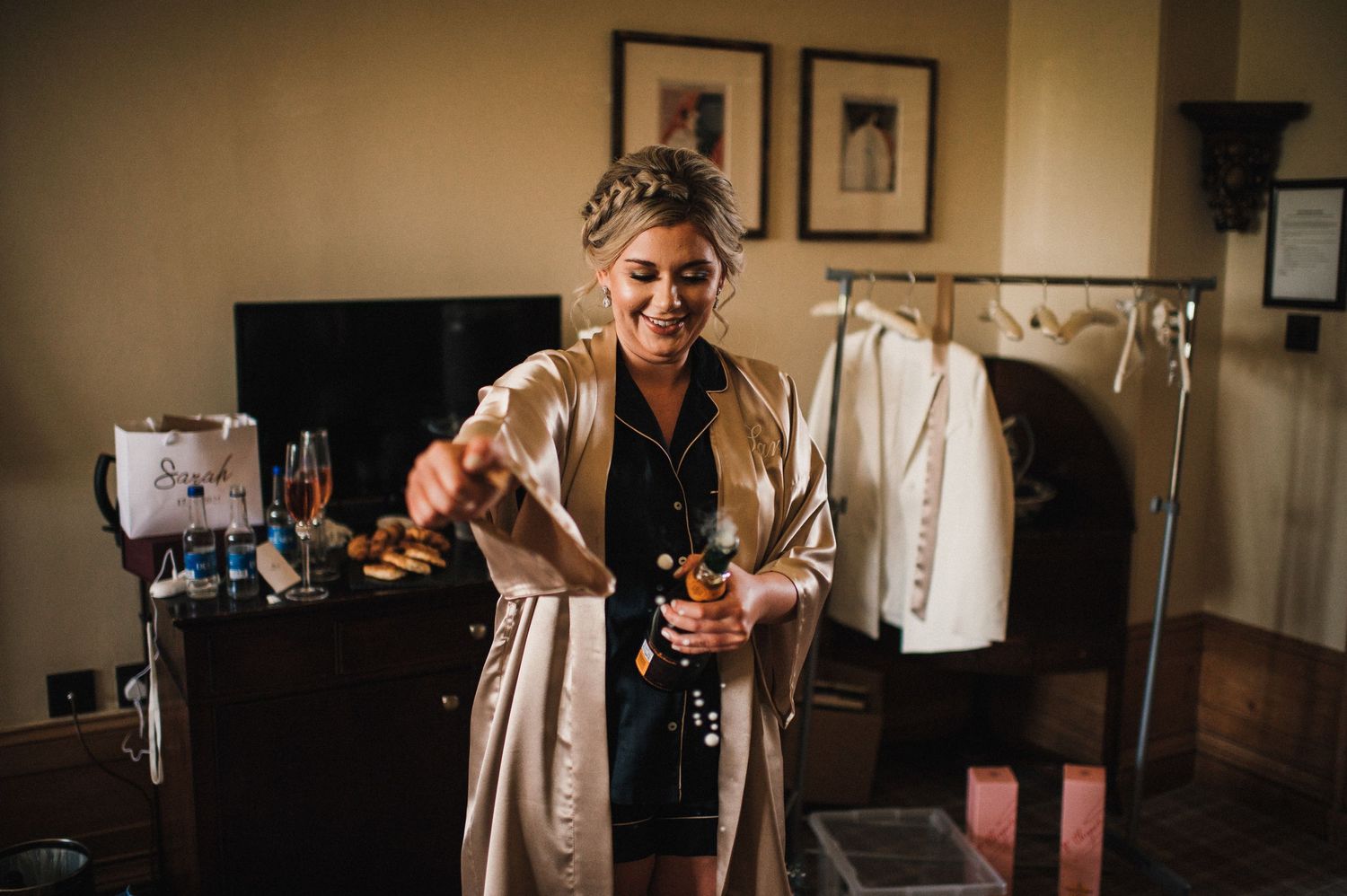 Person in silk robe stands near clothing rack during wedding preparations.