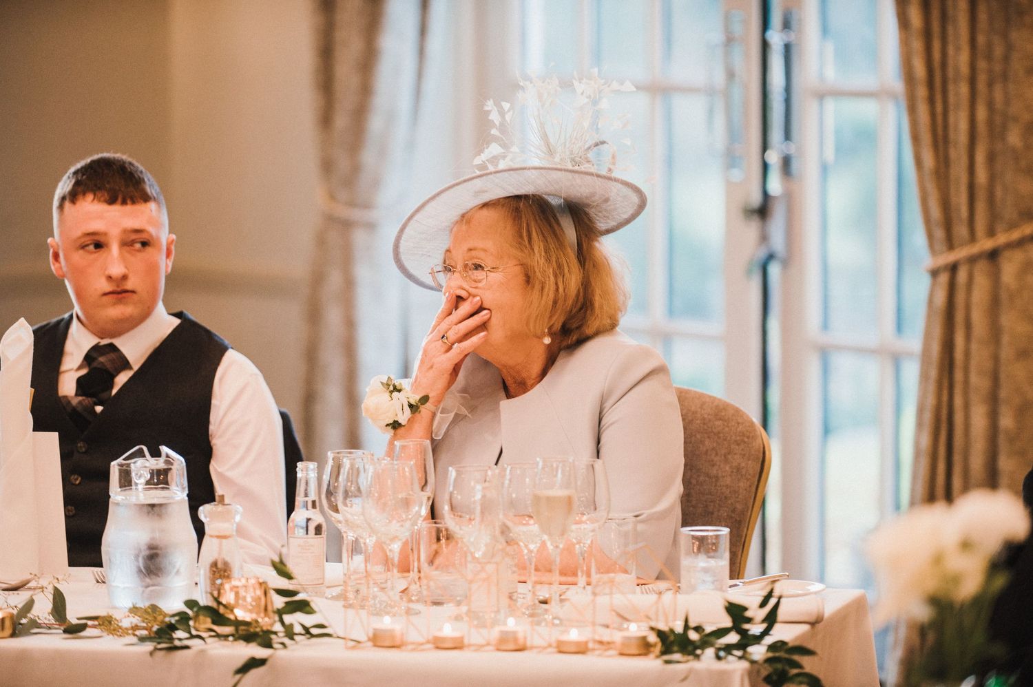 Guests share a lighthearted moment during a wedding reception speech at an elegant venue.