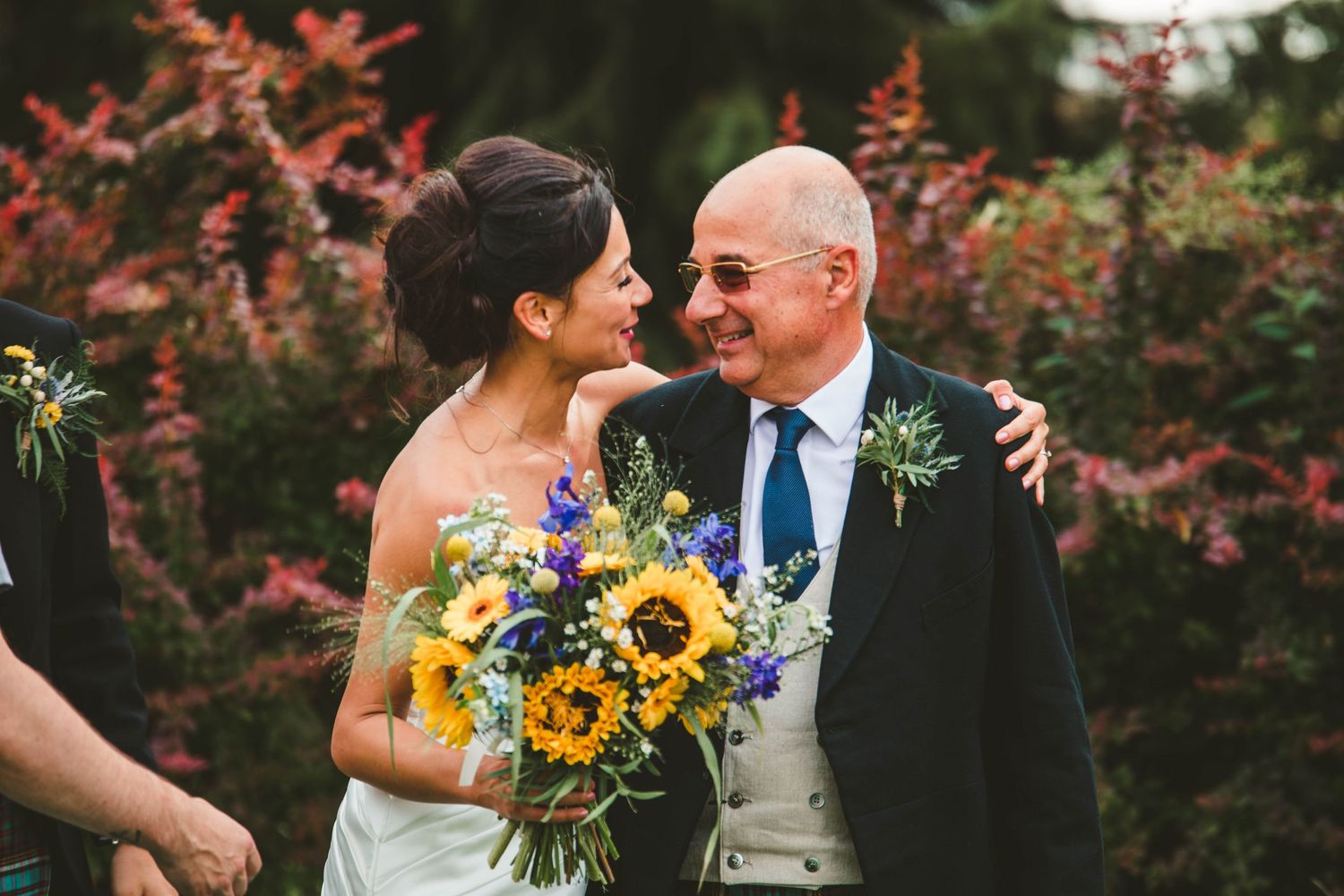 Candid moment between people at wedding with sunflower bouquet against autumn foliage.
