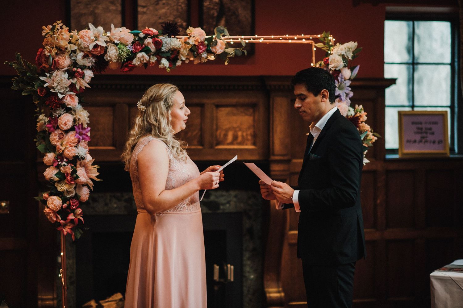 An intimate wedding ceremony moment under an ornate floral arch with pink and white flowers.