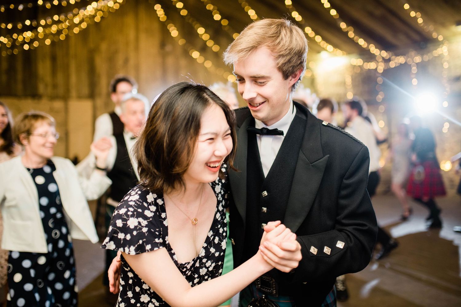 Guests share a joyful dance moment under string lights at a wedding reception.