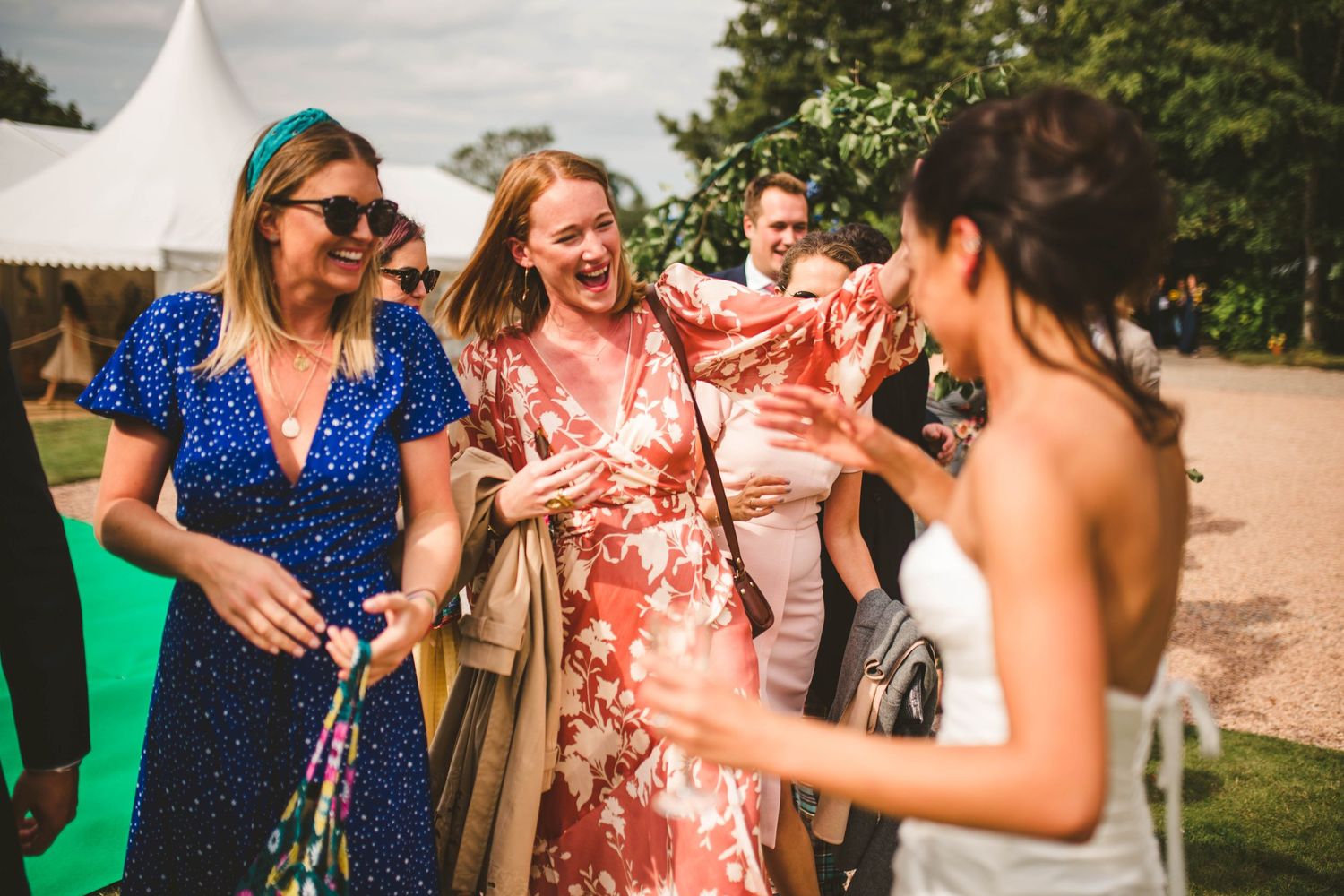 Wedding guests in colorful dresses share laughs during outdoor celebration.