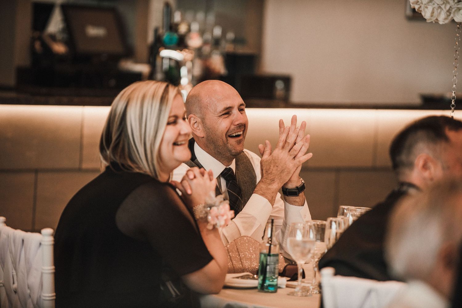 Wedding guests share a joyful laugh during celebration dinner at reception.