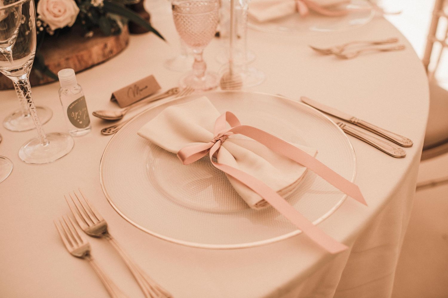 Elegant place setting with pink bow napkin and white dinnerware at wedding reception.