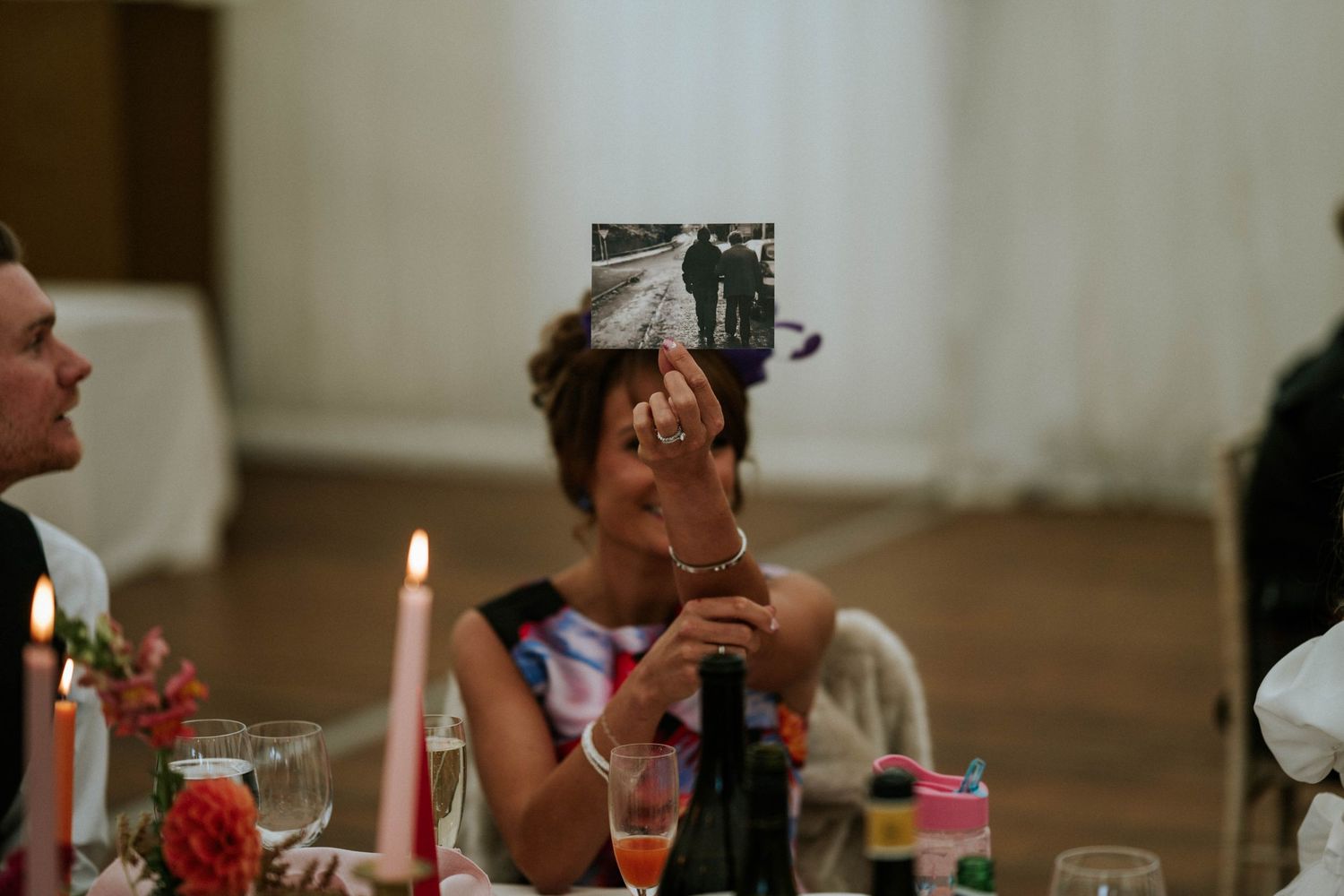 Wedding reception tables set with elegant decor and red floral arrangements in a white tent venue.