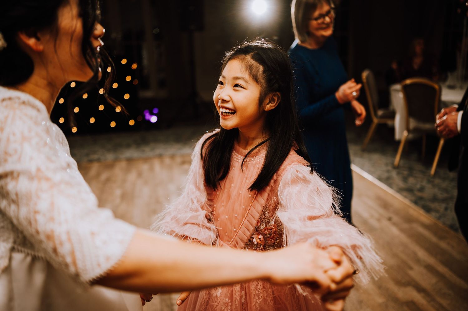 Two people holding hands while dancing at a festive celebration with warm lighting.