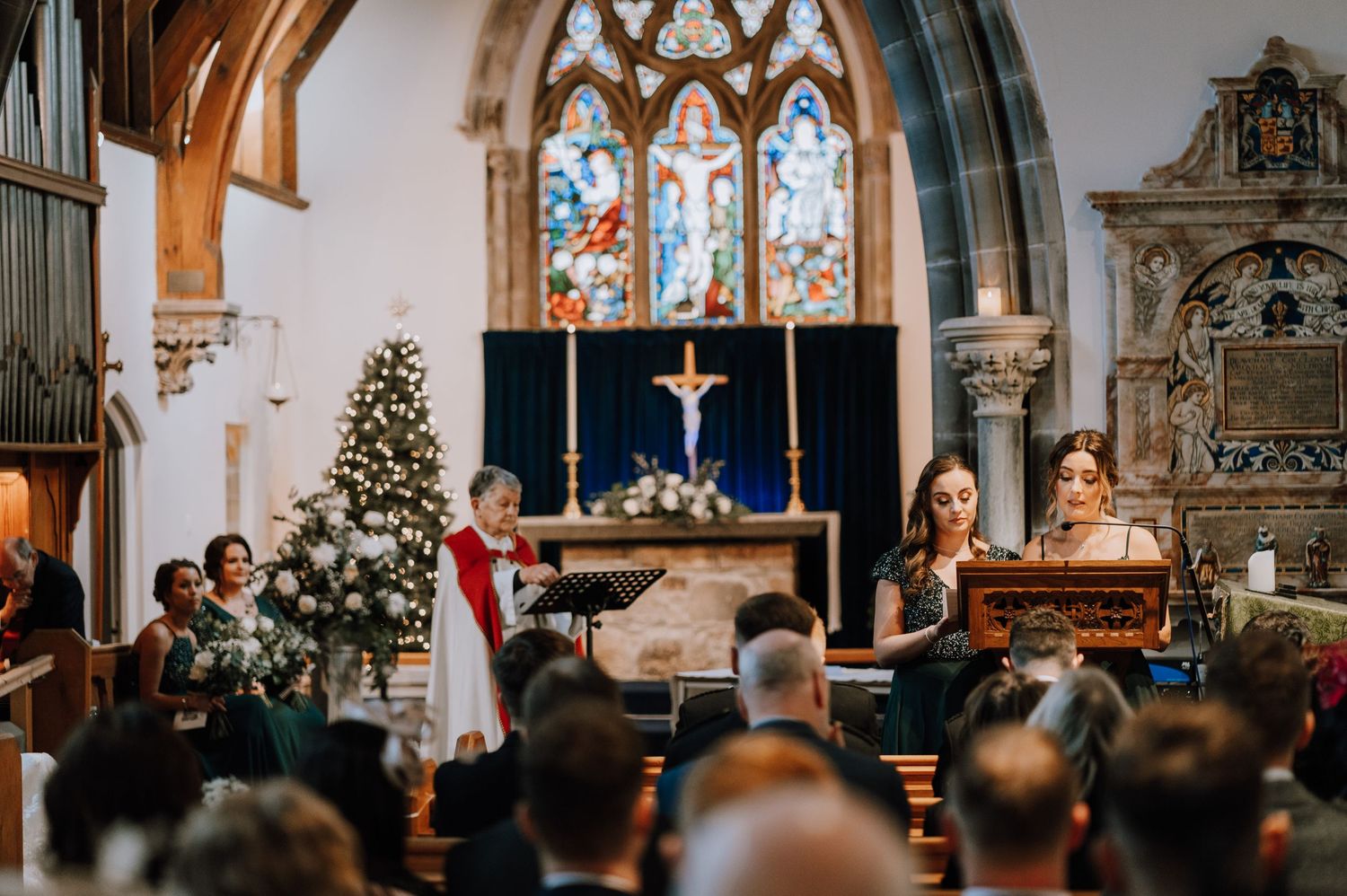 A Christmas wedding ceremony in a church with decorated tree and stained glass windows.