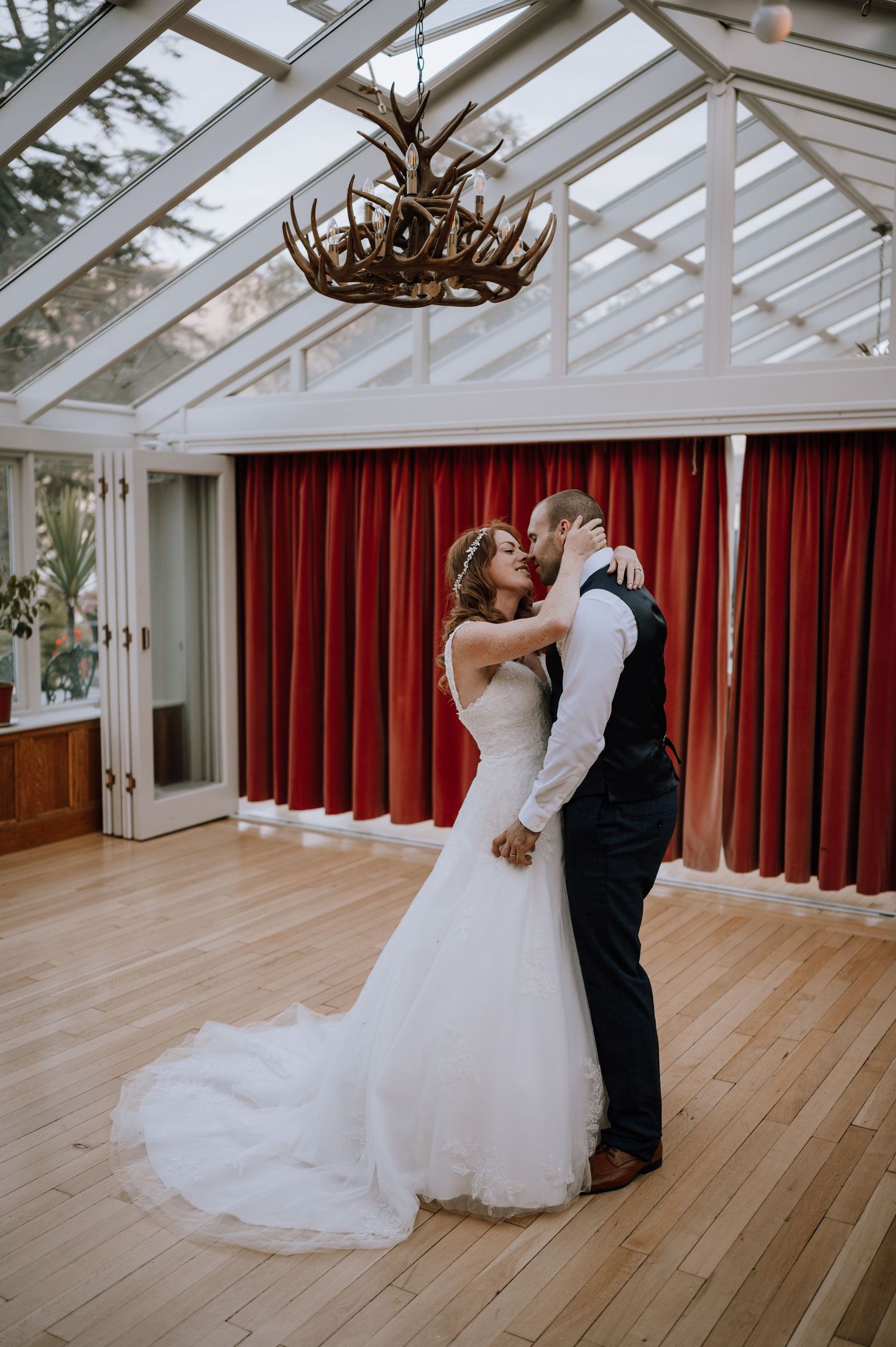 A romantic dance moment in an elegant glass-roofed conservatory with antler chandelier.