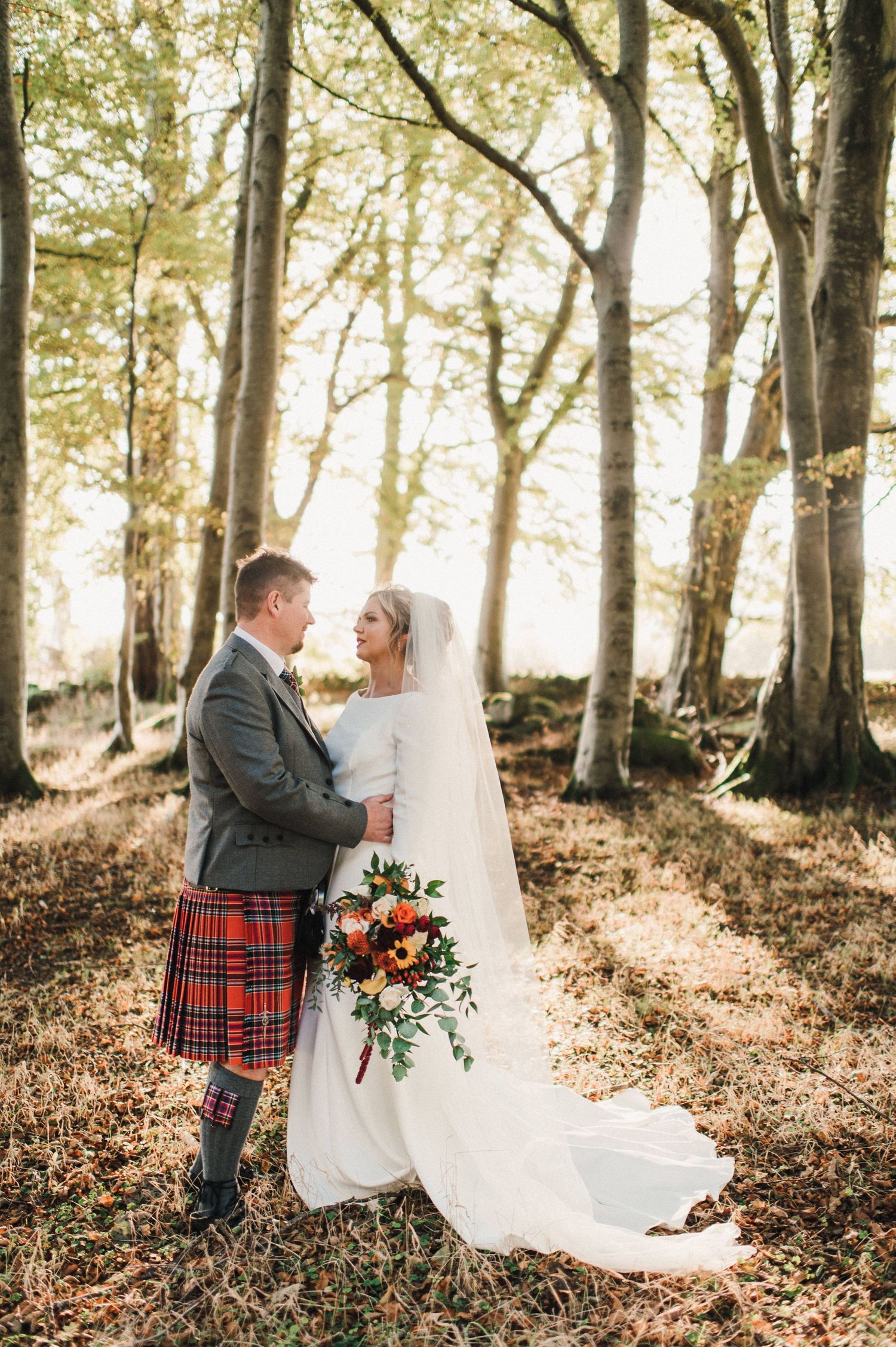 Wedding portrait in sunlit forest with autumn leaves and natural lighting.