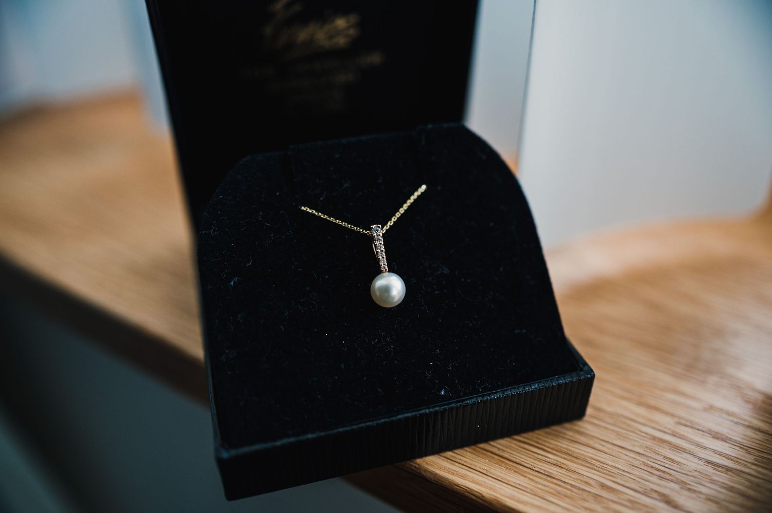 A delicate pearl pendant necklace displayed in a black jewelry box on a wooden surface.