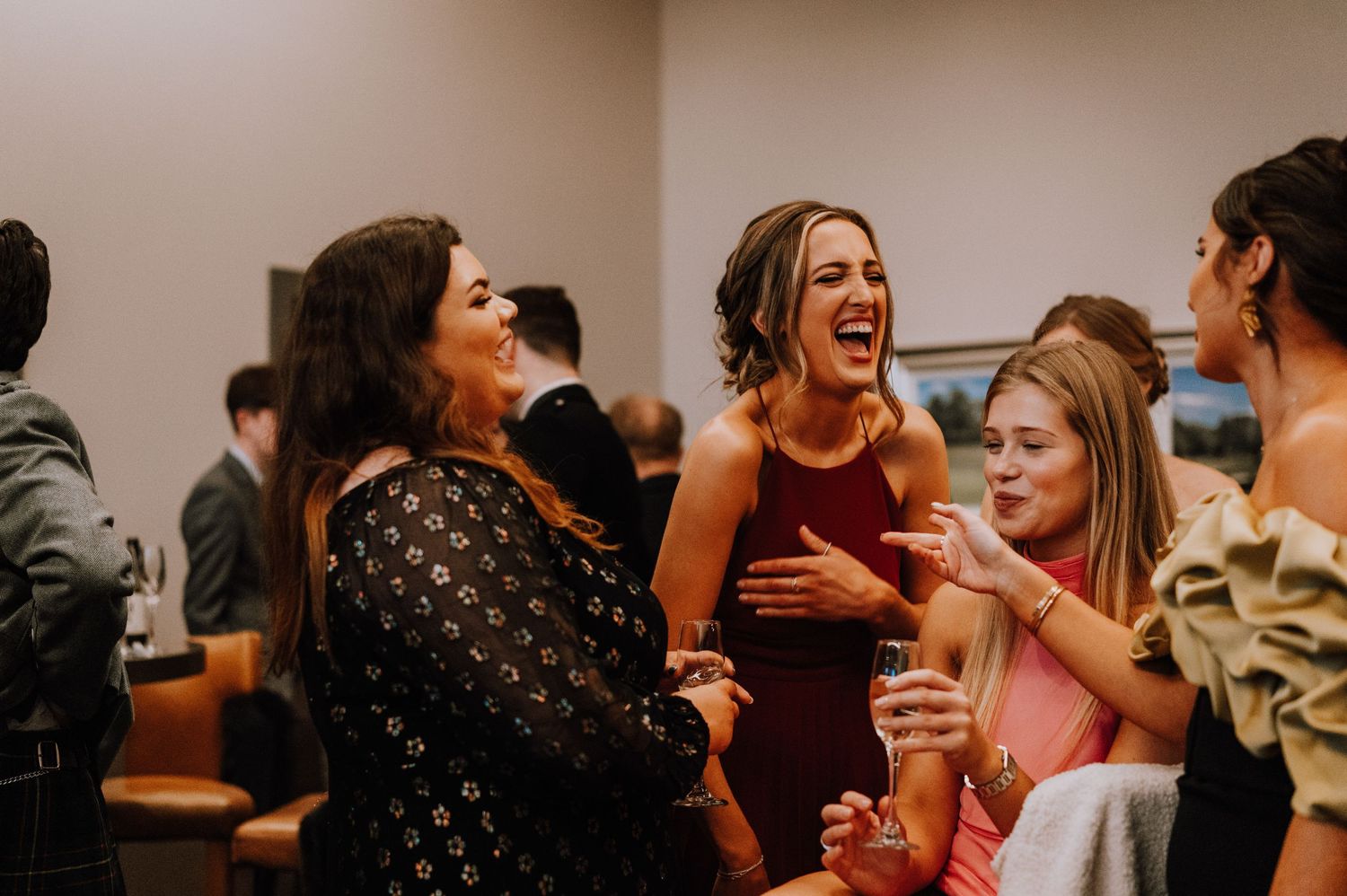 Friends in formal attire share a joyous moment while holding drinks at a celebration.