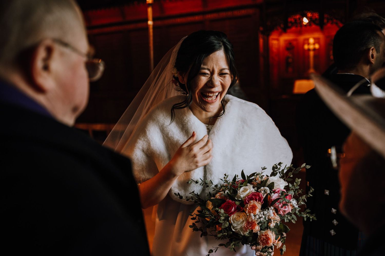 Winter bride in white coat holds colorful bouquet during reception celebration.