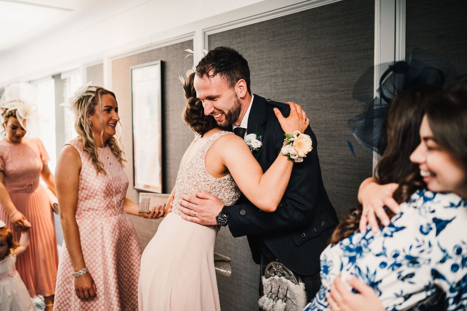 Wedding guests embrace during an emotional moment at an indoor celebration.
