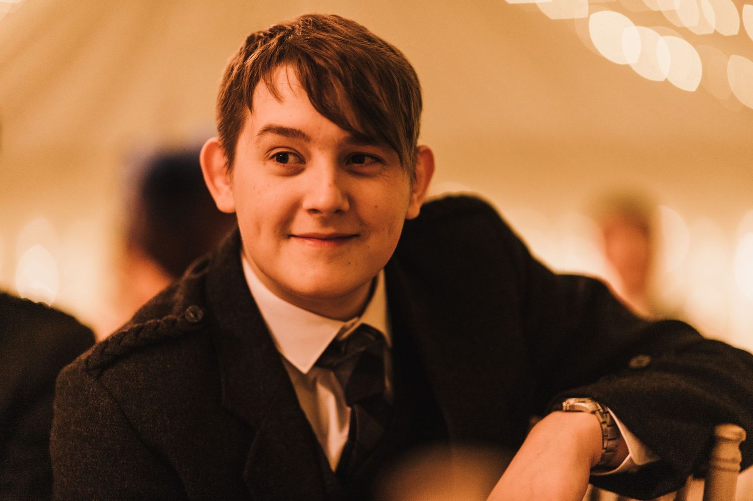 A guest in formal attire smiling at a wedding reception under warm lighting.