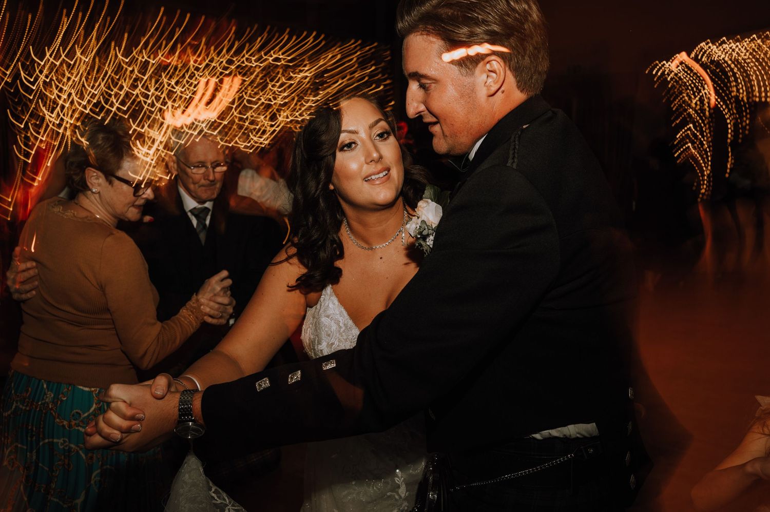 Couples dance together during a romantic evening reception with warm lighting effects.