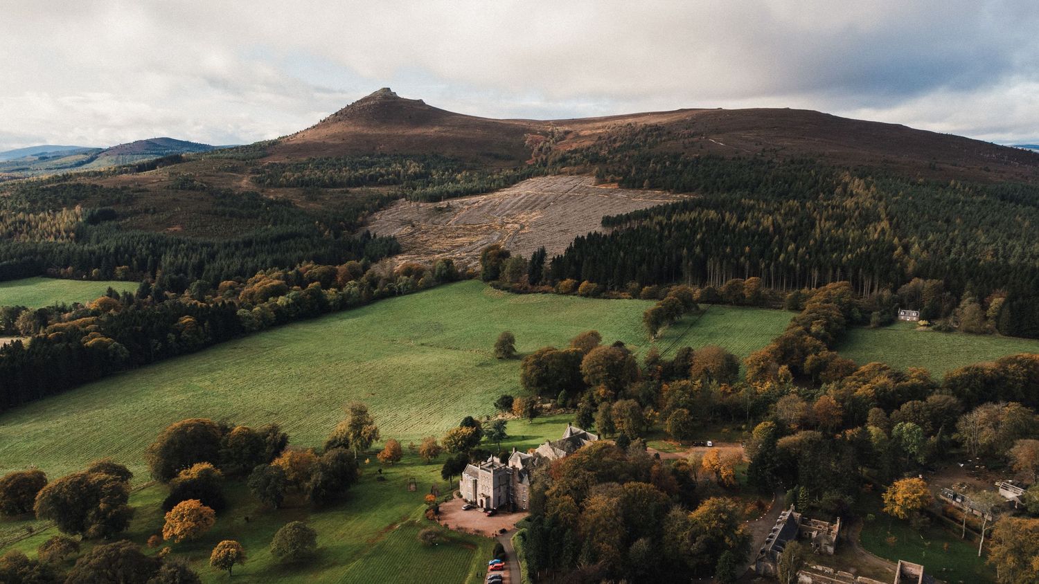 Drone shot of a historic building nestled among rolling hills and autumn forests.