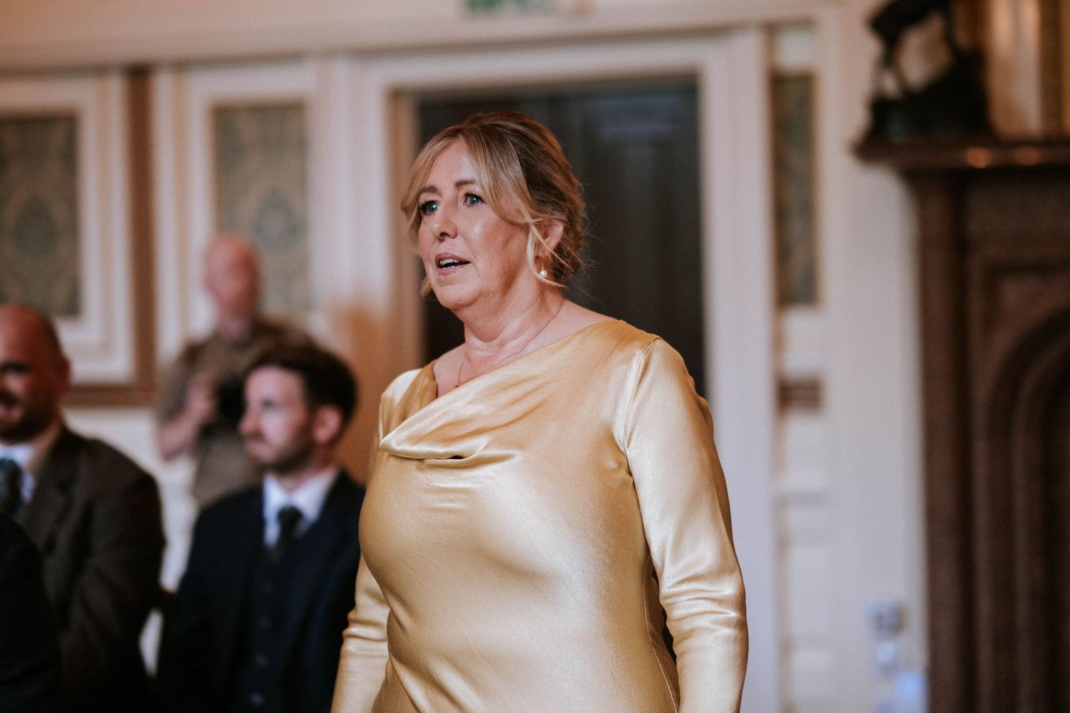 A person wearing a champagne-colored satin dress stands in an elegant interior setting.