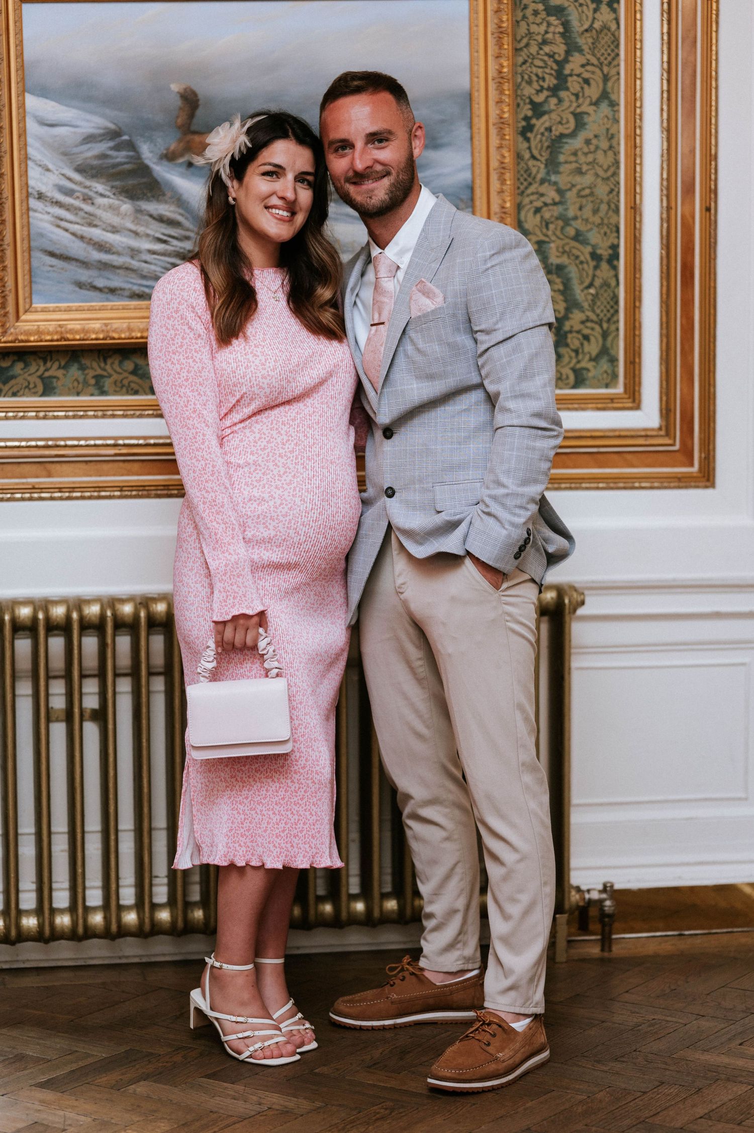 Couple poses in formal attire against elegant wallpaper and framed artwork.