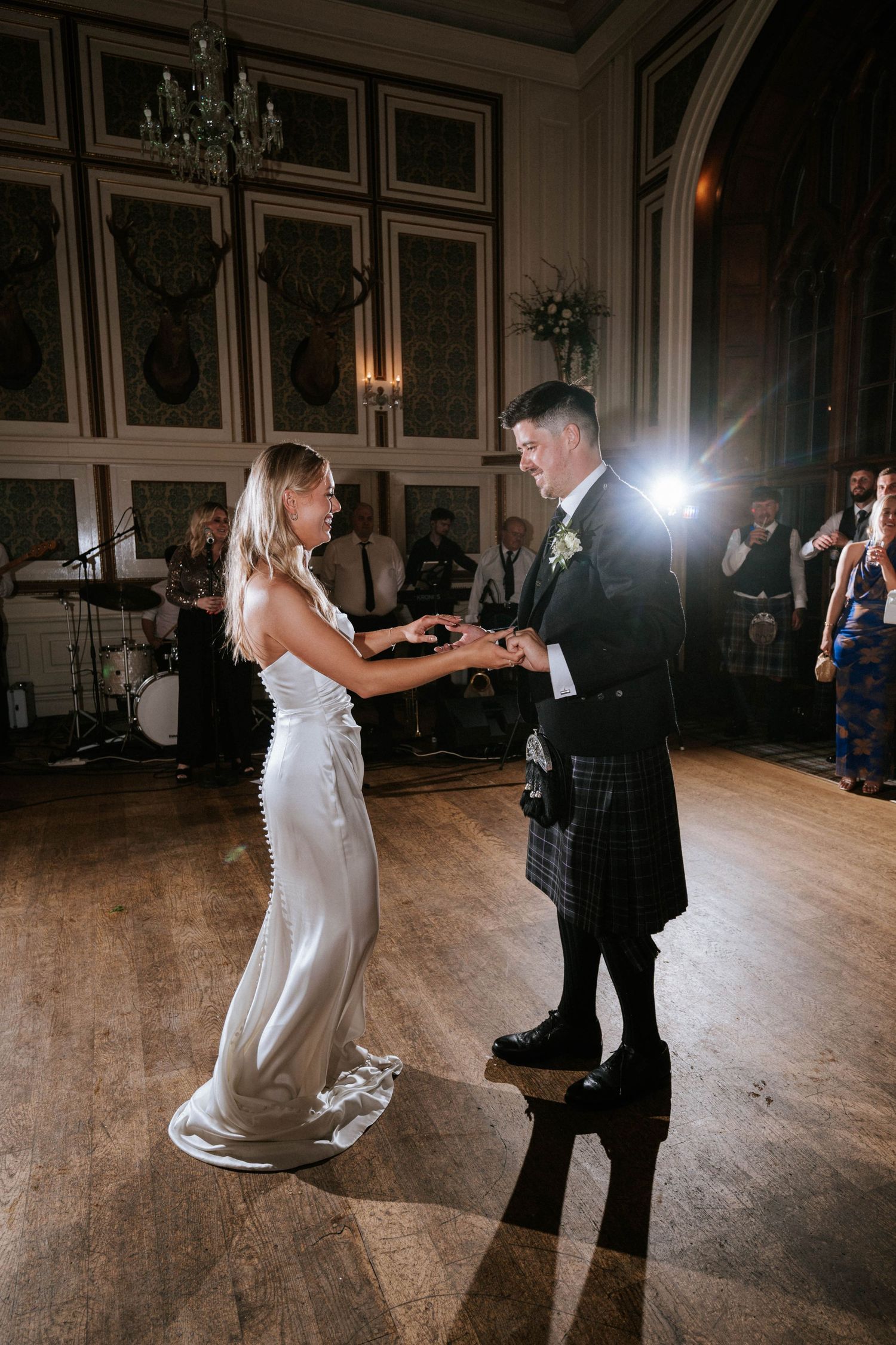 Wedding couple dancing together in an elegant ballroom with chandeliers and ornate wall paneling.